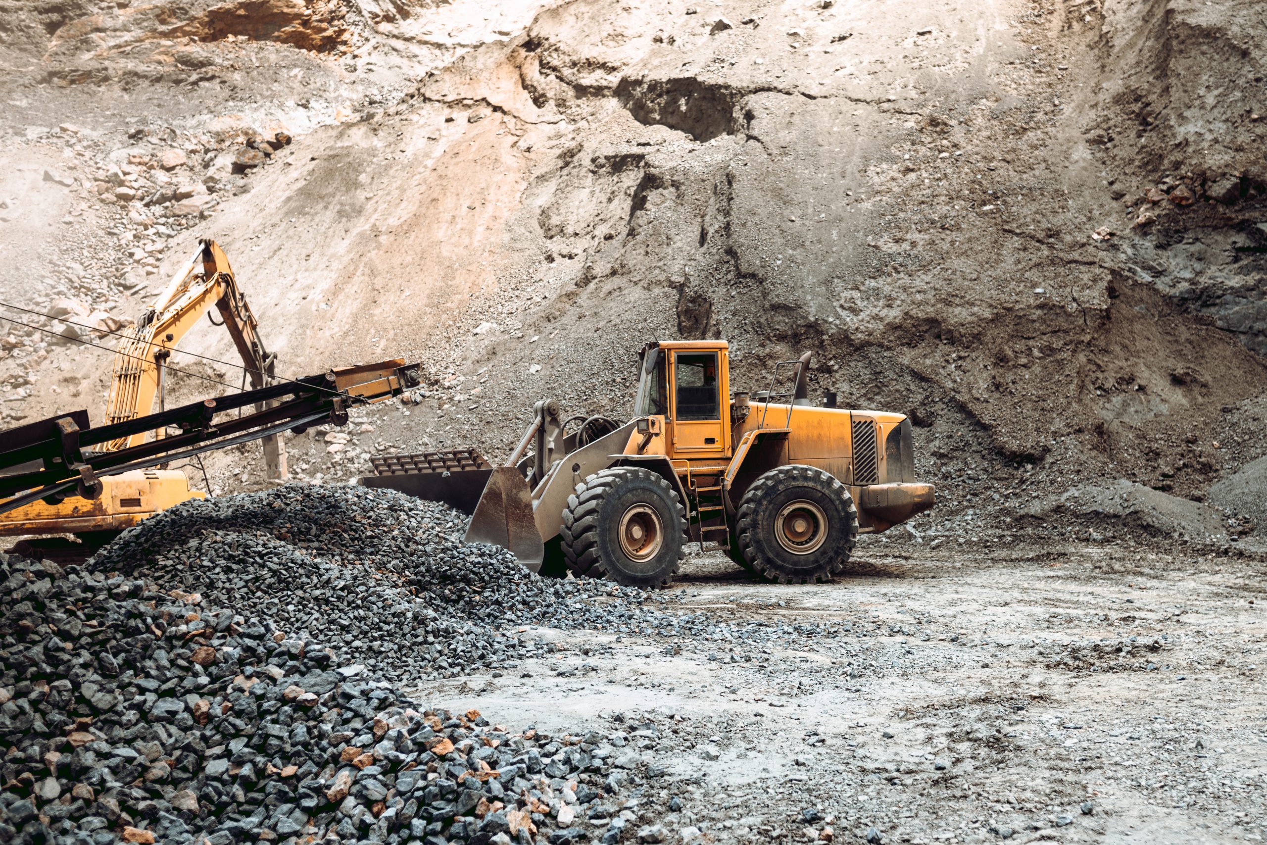 Industrial machinery on ore quarry site, heavy duty excavator moving gravel and rocks. Loading dumper trucks and rock crusher