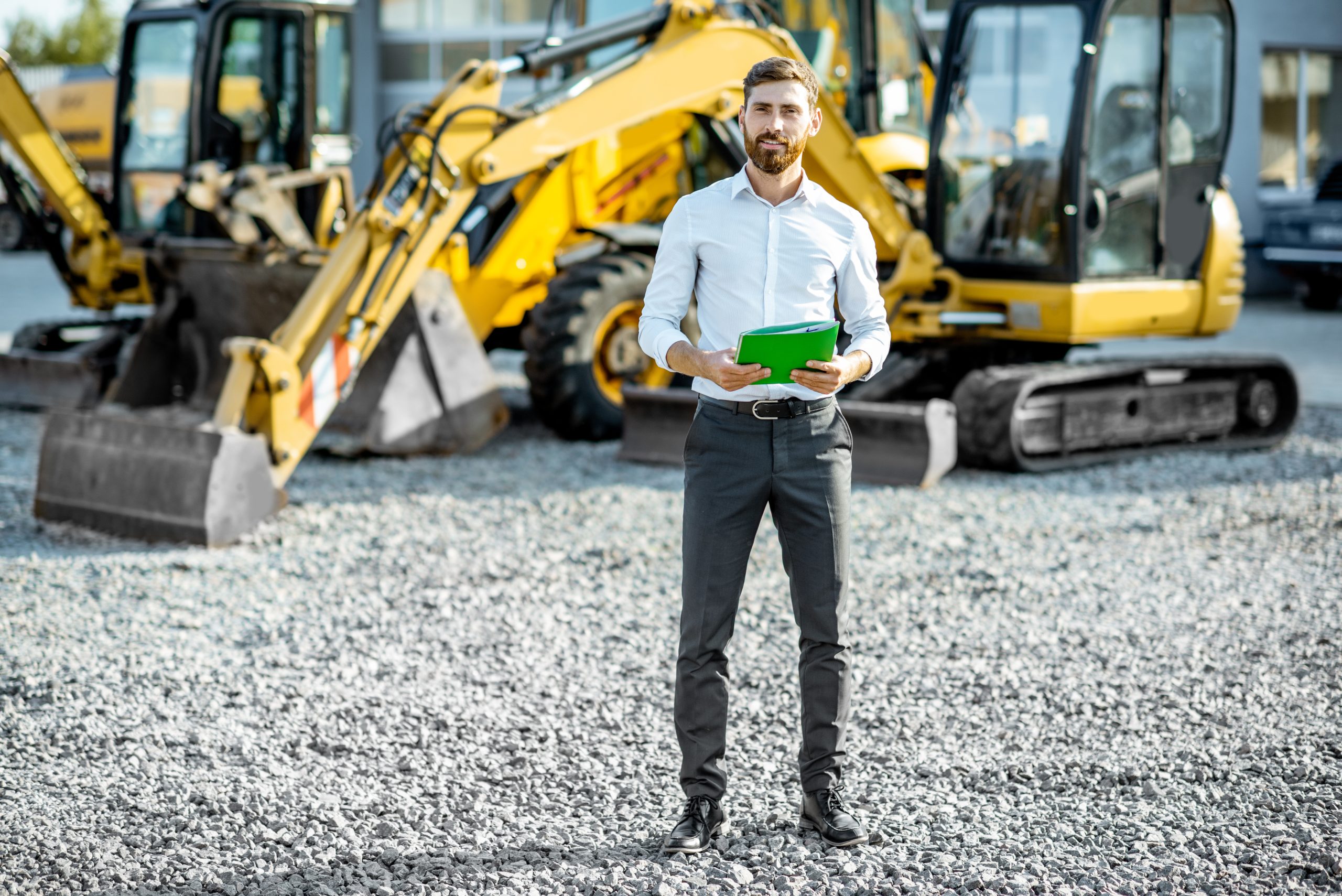 Portrait of a handsome sales consultant or manager standing on the open ground of the shop with heavy machinery for construction